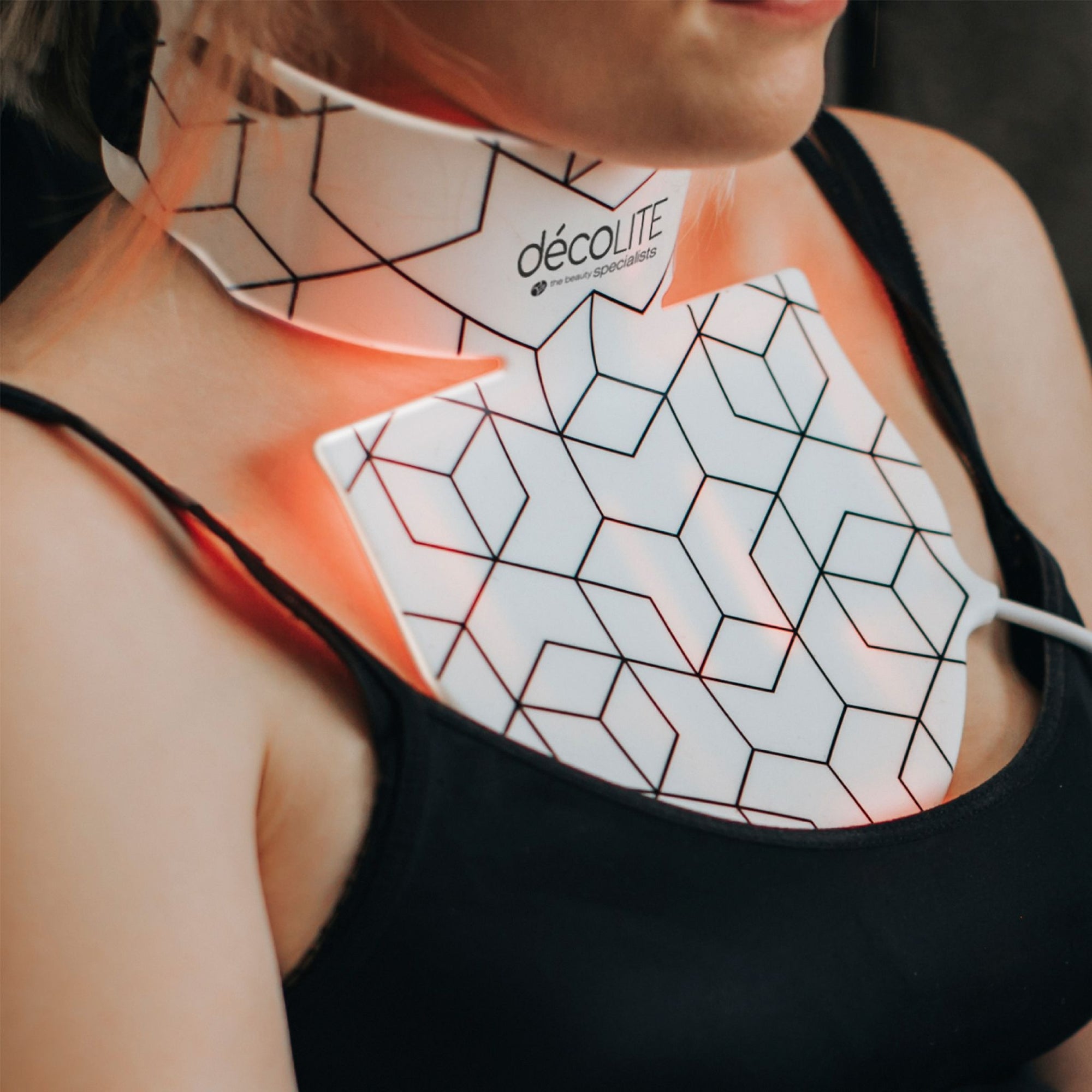 decoLITE LED light treatment being worn around neck and upper chest of female sat down on sofa.