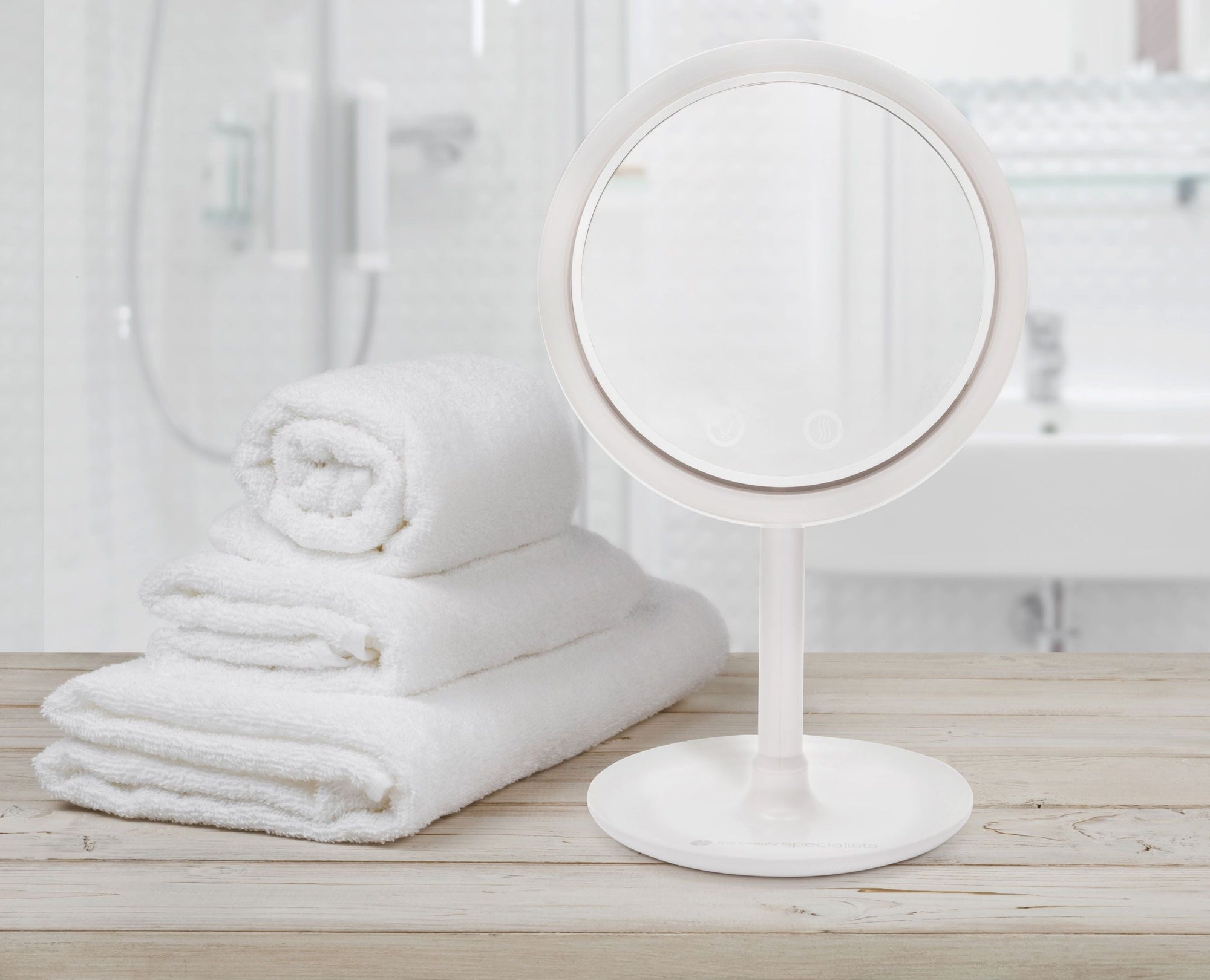 keep cool mirror with fan & led light ring placed on ledge in bright bathroom setting with while fluffy folded towels 