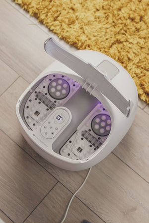 Deluxe steam foot spa on floor in home setting with splash cover lifted and purple lights illuminated 