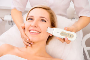 smiling lady laid back on treatment bed receiving ultrasonic facial treatment by beauty therapist