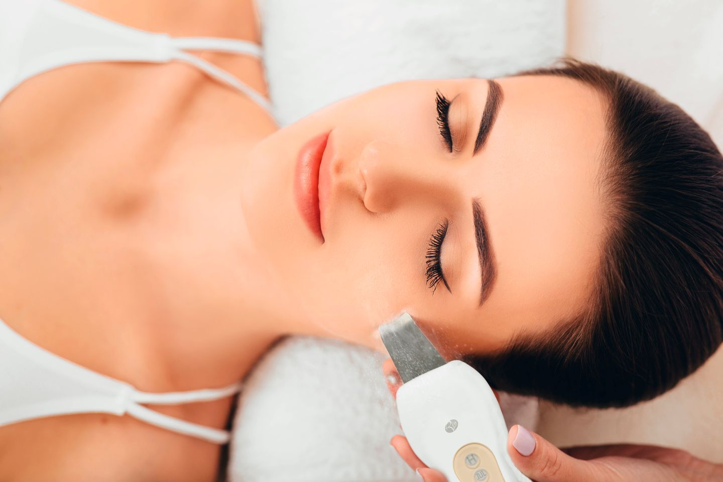 lady laid down receiving ultrasonic facial treatment with visible dead skin cells being removed by the ultrasonic vibrations 