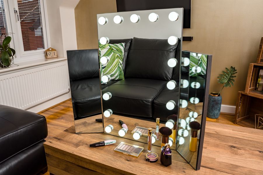 premier hollywood mirror with 20 LED lights and folding side mirrors stood on dressing table with LED lights illuminated and surrounded by cosmetics 
