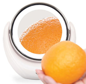 magnifying illuminated cosmetic mirror with orange held in front of it to demonstrated how the mirror magnifies the texture of the orange peel